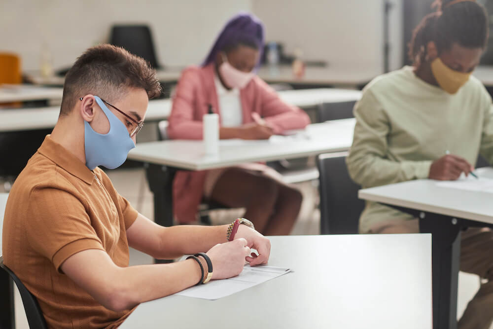 Happy graduate student with a certificate after graduation ceremony at the university. Side view portrait of young man wearing mask while taking test or exam in school with diverse group of people, copy space, Side view portrait of young man wearing mask while taking test or exam in school with diverse group of people, copy space