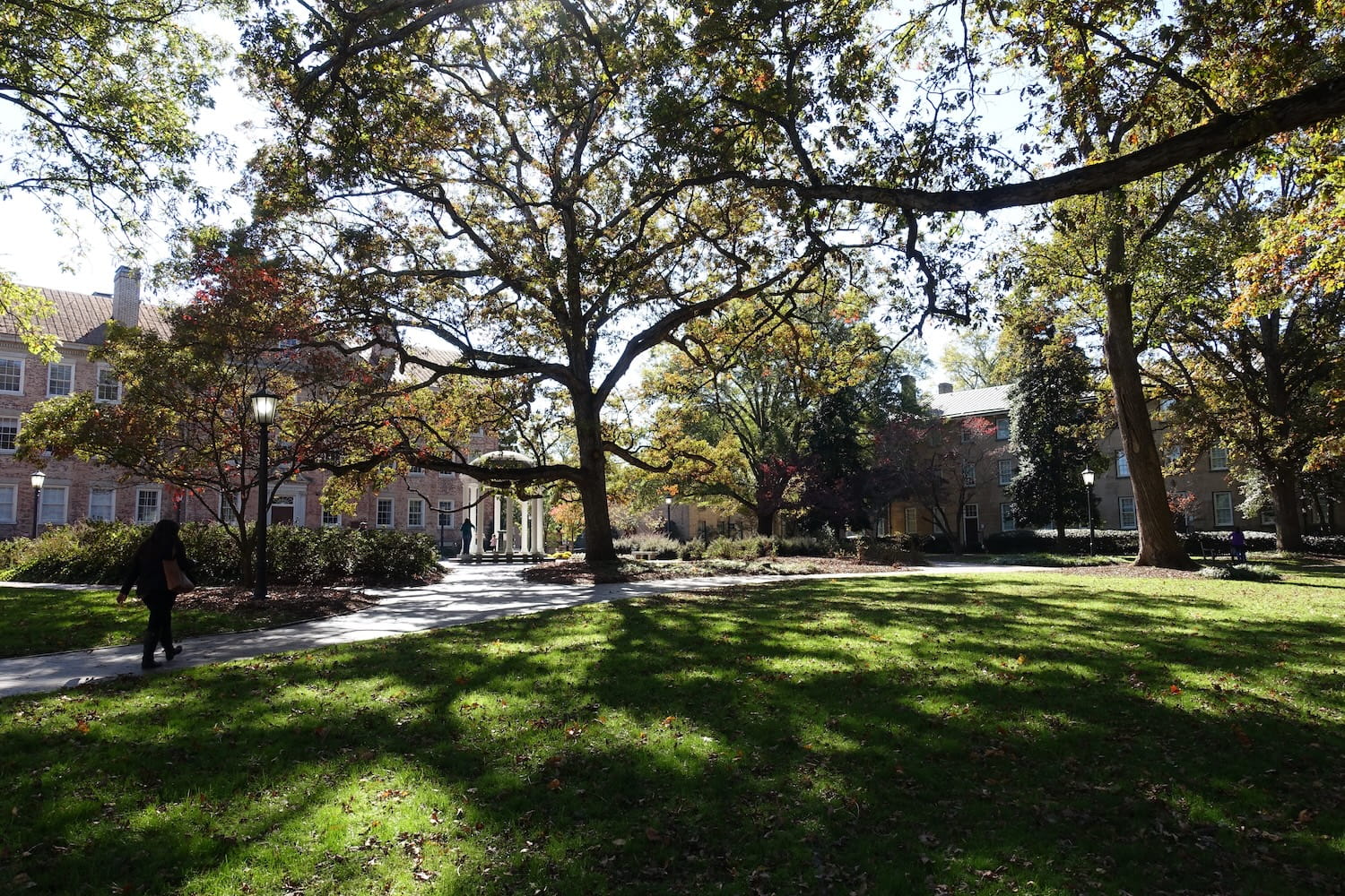 Happy graduate student with a certificate after graduation ceremony at the university. Brick academic buildings frame a tree-lined manicured lawn and walking paths at University of North Carolina's Chapel Hill, NC.