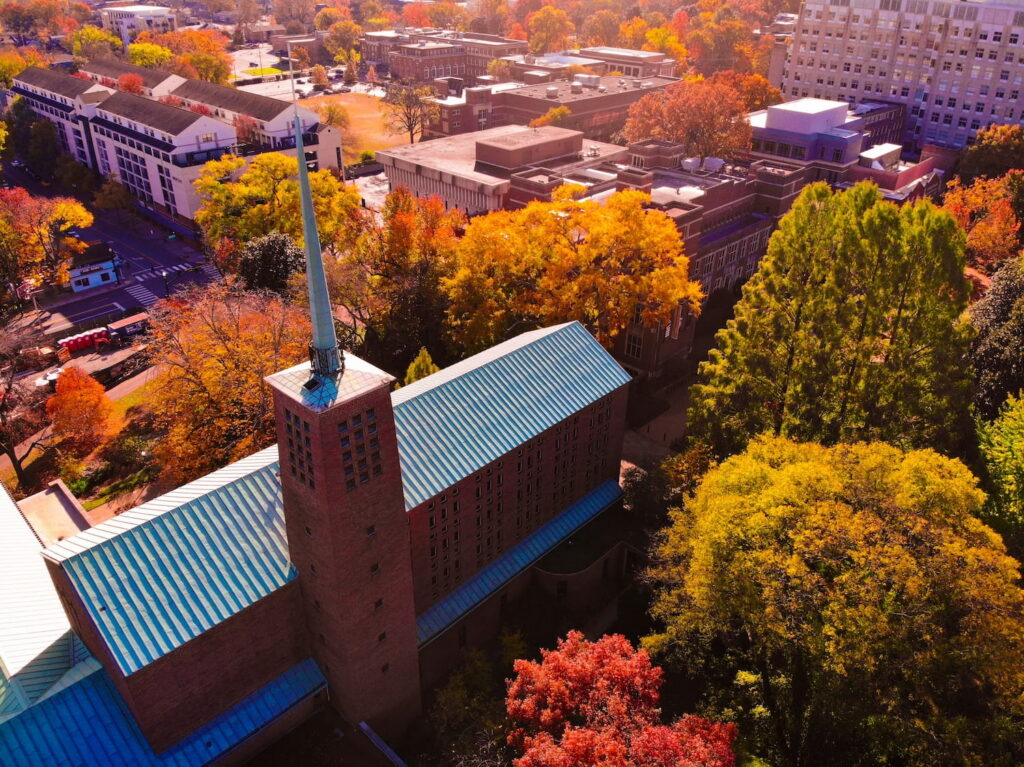 Happy graduate student with a certificate after graduation ceremony at the university. Aerial view of the brick General Theological Seminary building with fresh blue metal roofs, surrounded by autumn foliage at Vanderbilt University.